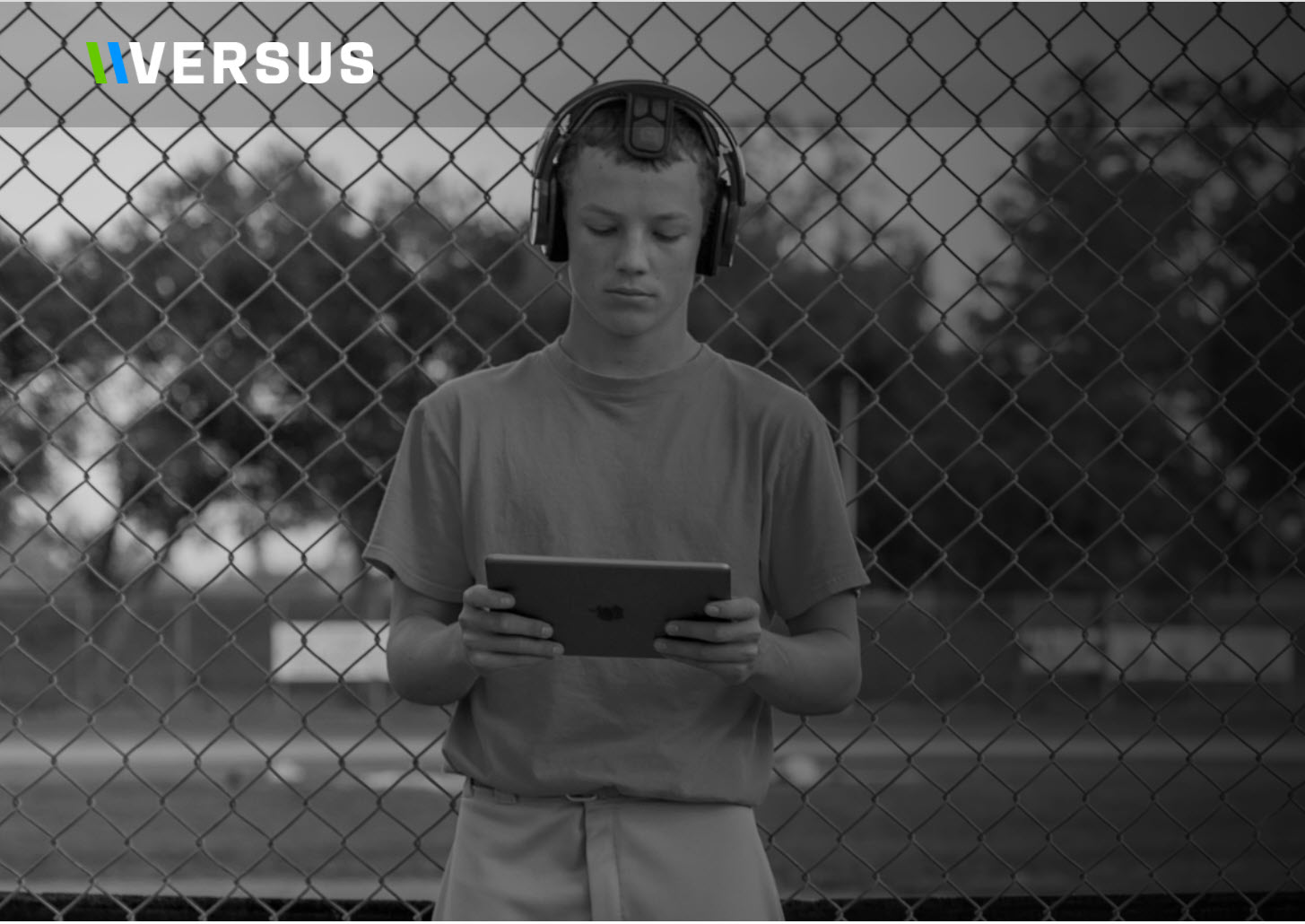 Young baseball player wearing a Versus EEG headset and using a tablet beside a chain-link fence